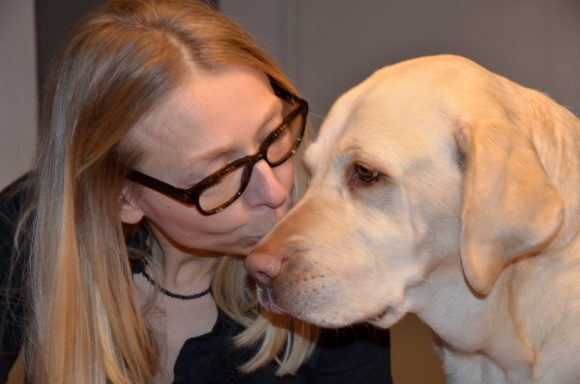 Eine blonde Frau küsst sanft einen gelben Labradorhund.