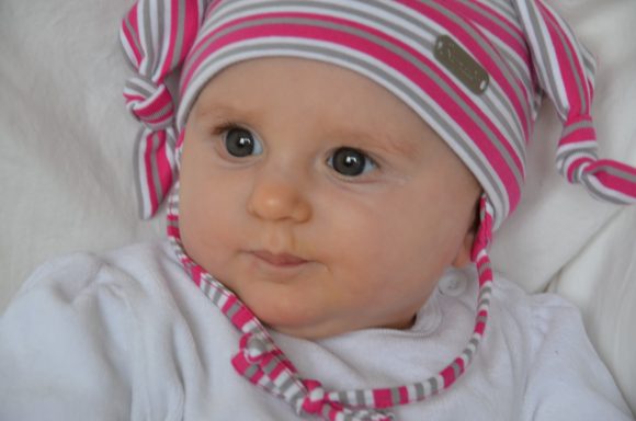 Ein Baby mit großen, blauen Augen und einem gestreiften Hut in rosa und Grau.