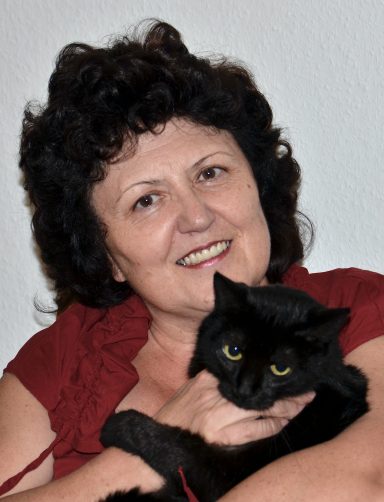 Frau mit lockigem, schwarzem Haar hält eine schwarze Katze in den Händen.