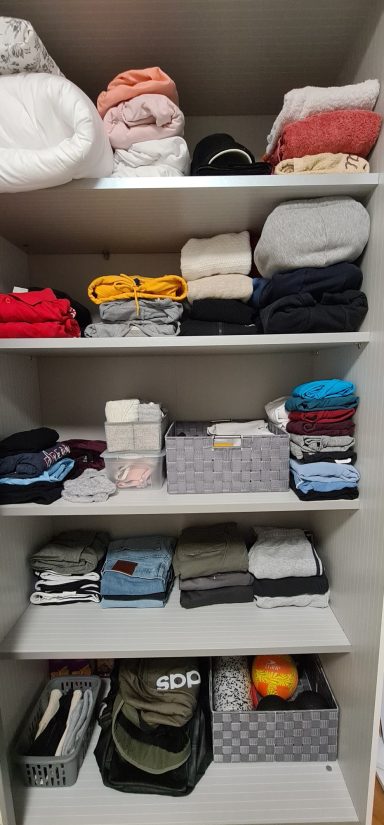 Ein geordneter Kleiderschrank mit gefalteten Kleidungsstücken und Aufbewahrungsboxen.